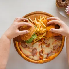 Mani che afferrano un hamburger, patatine, nuggets e pizza. Un vero **cheat day** con ciambelle in lontananza.