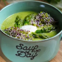 Aksamitna zupa z zielonych szparagów, udekorowana kiełkami i kleksem śmietany, w ceramicznej misce z napisem "Soup of the Day".