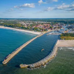 Widok z lotu ptaka na port w Ustce z falochronami, plażą i miastem w tle.