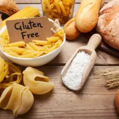 Różne rodzaje makaronów i pieczywa, a także mąka i kłosy zbóż. Etykieta "Gluten Free" sugeruje dyskusję: czy gluten jest zdrowy?