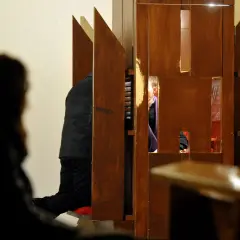 W konfesjonale klęczy mężczyzna, a za kratkami widać księdza. Czy konieczna jest spowiedź przed chrztem?