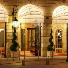 Eleganckie wejście do słynnego paryskiego hotelu Ritz, oświetlone latarniami i ozdobione spiralnymi drzewkami.