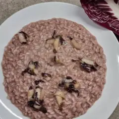 Un cremoso risotto al radicchio, con pezzetti di verdura che spuntano, accanto a una foglia fresca di radicchio.