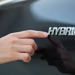 Dłoń dotyka znaczka "HYBRID", symbolizując rozważania nad silnik hybrydowy wady i zalety.