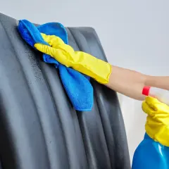 Ręka w żółtej rękawiczce czyści czarną ekoskórę niebieską ściereczką. Dowiedz się, czym czyścić ekoskórę, by zachować jej piękny wygląd.