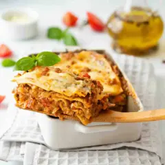 Une part généreuse de lasagne, digne d'une recette de chef italien, est servie. Tomates et basilic frais décorent ce plat réconfortant.
