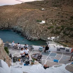 Människor njuter av en måltid på en terrass med utsikt över en vik på Sifnos, Grekland.