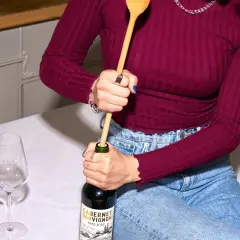 Korken ohne Korkenzieher: Eine Person versucht, eine Weinflasche mit einem Holzlöffel zu öffnen.