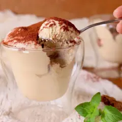 Un cucchiaino preleva una porzione generosa di soffice mousse al caffè, cosparsa di cacao, da un bicchiere di vetro.