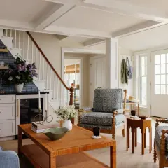 A living room with a traditional style, featuring blue patterned armchairs, a rattan coffee table, and a bar area with blue tiled backsplash.