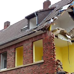 Zniszczony budynek z cegły, dach w trakcie rozbiórki. Jeśli planujesz wyburzenie budynku, sprawdź, gdzie zgłosić wyburzenie budynku.