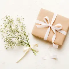 Bukiet gipsówki z kremową wstążką i prezent w papierze kraft, ozdobiony jasnoróżową wstążką. Czy kwiaty daje się w papierze? Tak, w takim eleganckim opakowaniu.
