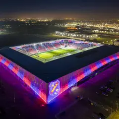 Nowoczesny stadion Odra Opole nocą, oświetlony na czerwono i niebiesko.