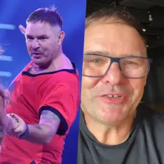 Tomasz Karolak tańczy na scenie w czerwonej koszulce i pozdrawia z uśmiechem w okularach. Obok niego uśmiechnięta kobieta.