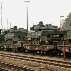 Pociąg wojskowy transportuje kilka czołgów Leopard 2 na wagonach platformach.