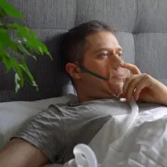 Mężczyzna w masce tlenowej leżący w łóżku.