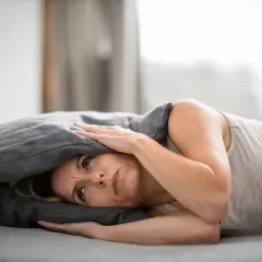 Frau mit Kissen über dem Kopf, die unter Tinnitus leidet und nach Linderung durch Osteopathie sucht.