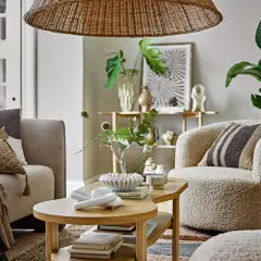 Przytulny salon w stylu skandynawskim: beżowa kanapa, puszysty fotel, drewniany stolik z dekoracjami i pleciony klosz lampy.