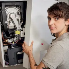 Une technicienne installe une chaudière F28. Elle tient le panneau avant ouvert, révélant les composants internes.