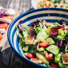 Kolorowa sałatka z pomidorkami, ogórkiem i grzankami, idealna na dietę low carb. Obok caprese.