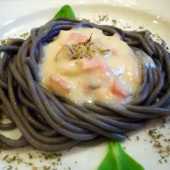 Espaguetis negro con nata, trocitos de jamón y hierbas aromáticas, servido en un plato blanco.
