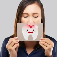 Donna con gli occhi chiusi mostra un disegno di un dente che cade, con espressione sofferente e macchie di sangue.