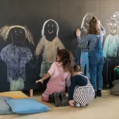 Dzieci rysują kredą na tablicy postacie, ćwicząc umiejętności emocjonalne i społeczne.