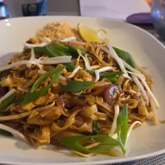 Pad thai z kurczakiem, kiełkami fasoli mung, szczypiorkiem i ćwiartką limonki na białym talerzu.