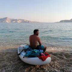Chorwacja: mężczyzna na desce SUP na kamienistej plaży, w tle góry i spokojne morze. Idealne miejsce na relaks.