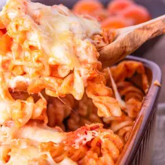 Un cucchiaio solleva un'abbondante porzione di pasta alla sorrentina filante, con pomodoro e mozzarella dorata.