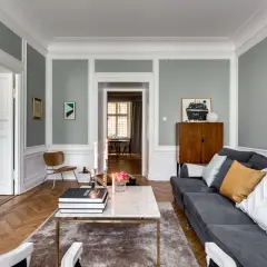 Ett stilrent vardagsrum med grå väggar, vita snickerier och en maffig soffa. Perfekt inspiration om du vill måla väggar själv.