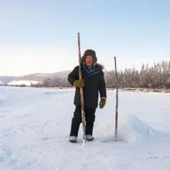 Mężczyzna w futrzanej czapce i ciepłej kurtce stoi na mroźnym, zaśnieżonym polu. To surowa, piękna syberia zimą.