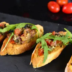 Cztery chrupiące bruschetty z pomidorami, ziołami i rukolą, idealne jako tapas.