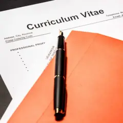 Eleganckie pióro na tle dokumentu Curriculum Vitae po angielsku i pomarańczowej koperty.