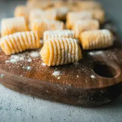 Gnocchi di patate fatti in casa, pronti per essere cucinati, disposti su un tagliere di legno scuro.