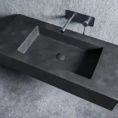 Nowoczesna umywalka z betonu o minimalistycznym designie, z wpuszczonym w blat odpływem i elegancką baterią ścienną.