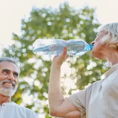 Un couple profite du soleil, la femme boit de l'eau pour une hydratation optimale, l'homme sourit.