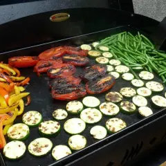 Poivrons, tomates, courgettes et haricots verts grillés sur une plancha. Une délicieuse pierrade végétarienne en préparation.