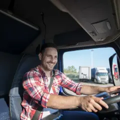 Uśmiechnięty kierowca w kratę za kierownicą ciężarówki. To jego dzień transportowca, gotowy na kolejną trasę.