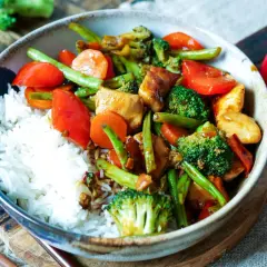 Schüssel mit Reis und buntem Chop Suey: Hühnchen, Brokkoli, Karotten, Paprika und grüne Bohnen in einer herzhaften Sauce.