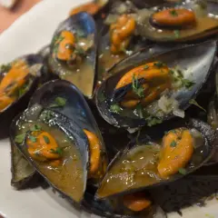 Un plato lleno de mejillones a la marinera, jugosos y con perejil picado, listos para disfrutar.