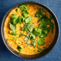 Ein dampfender Linsen-Curry in einer Schüssel, garniert mit frischem Koriander und Minze.