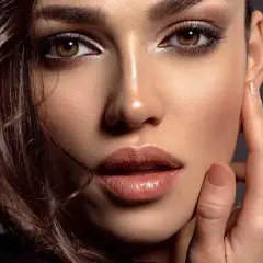 Primo piano di una donna con un sofisticato trucco occhi neri, labbra lucide e capelli castani mossi.