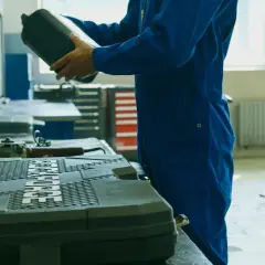 Meccanico in tuta blu prepara il cambio olio motore fuoribordo 4 tempi, tenendo una tanica di olio.