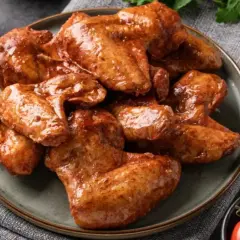 Sabrosas alitas de pollo a la coca cola, glaseadas y doradas, servidas en un plato con salsa y tomates cherry.