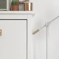 Un mueble blanco con un tirador de cuero y un altavoz Marshall. Una lámpara blanca con detalles de madera ilumina la escena.