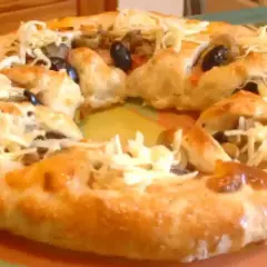 Pizza maison avec une croûte dorée, garnie d'olives noires et de fromage râpé. Parfait pour une recette pâte à pizza rapide.