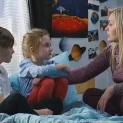 Kobieta z dwójką dzieci, otoczona plakatami kosmicznymi, rozmawia o przyczyny popularności motywu "found family" w literaturze przygodowej.