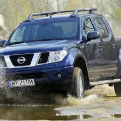Niebieski Nissan Navara pokonuje wodną przeszkodę, rozpryskując błoto.