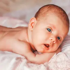 Niemowlę z niebieskimi oczami leży na brzuchu. Delikatny meszek, czyli lanugo, pokrywa jego plecy.